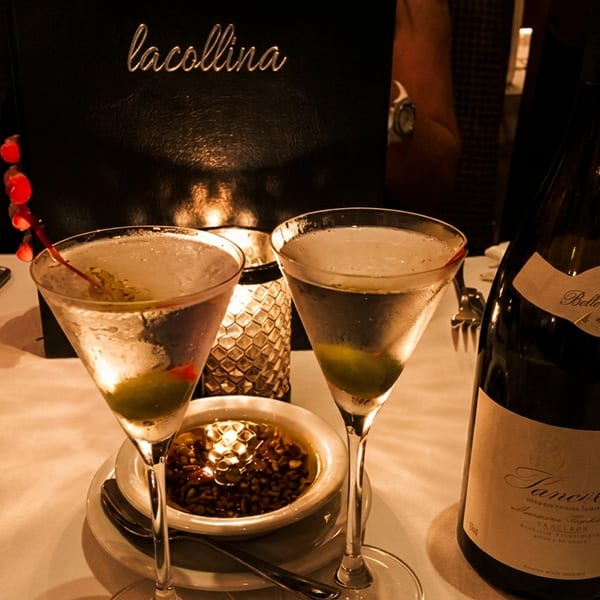 Two martinis, a bowl of olives, and a wine bottle on a white tablecloth at La Collina.